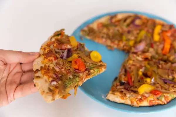 Ein Stück knusprig gebackene vegetarische Pizza von Garden Gourmet in der Hand und bereit zum Verzehr