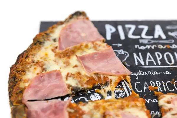 Ein Stück Pizza mit Prosciutto und schwarzem Pizzaboden in der Nahaufnahme