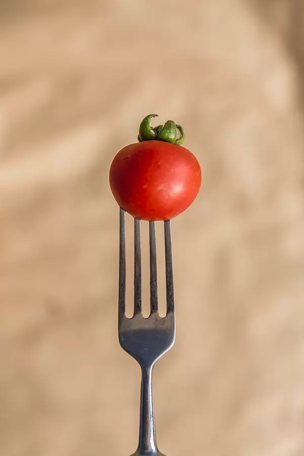 Ein vertikales Foto einer kleinen roten Tomate auf einer Gabel