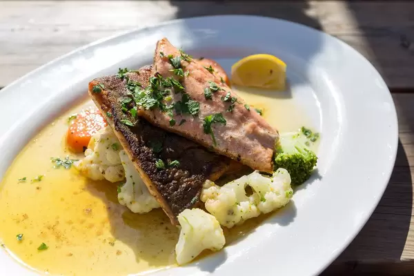 Ein weißer Teller mit Saibling, Blumenkohl, Brokkoli und Kräuter. Typischer Fisch von den Seen der Alpen
