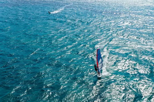 Ein Windsurfer und ein Kitesurfer im blauen Meer von Mikri Vigla, Naxos, Griechenland. Drohnenfoto