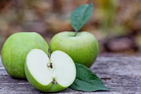 Eine Apfelhälfte mit zwei günen Äpfeln im Hintergrund
