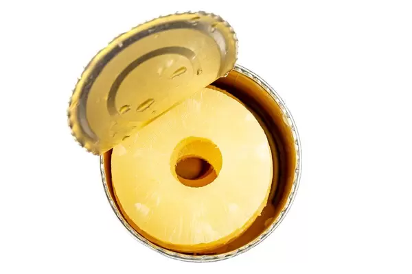 Eine Dose Ananas in Saft öffnen. Aufnahme von oben auf weißem Hintergrund