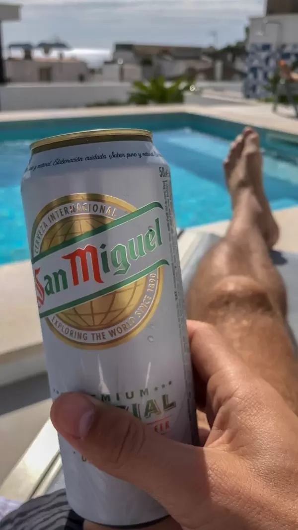 Eine Dose San Miguel Bier in der Hand eines Mannes der an einem Pool auf Mallorca entspannt