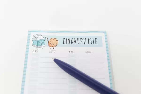 Eine Einkaufsliste schreiben, bevor man zum Supermarkt fährt: Notizblock und Kugelschreiber vor weißem Hintergrund