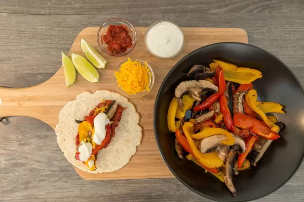 Eine Fajita mit Paprika und Pilzen, scharfer Soße, Cheddar und Limettenschmand auf einem Brettchen in der Aufsicht