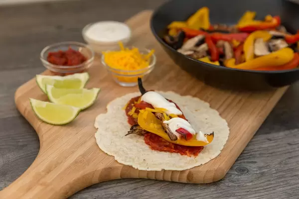 Eine Fajita mit Tomatenmark, Cheddar, Paprika und Pilzen und Limettenschmand auf einem Brettchen