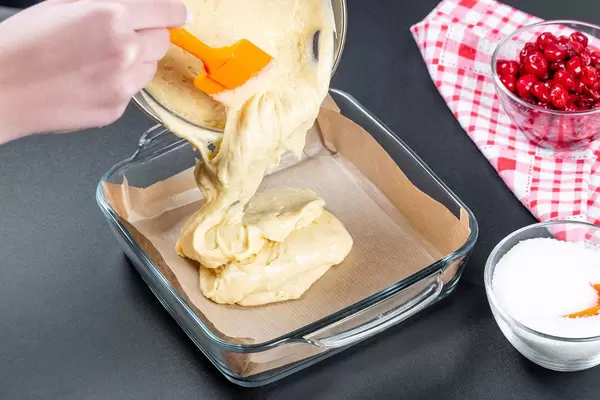 Eine Frau lässt den Teig in eine Glas-Backform fließen