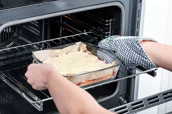 Eine Frau schiebt einen ungebackenen Kuchen in einen elektrischen Backofen