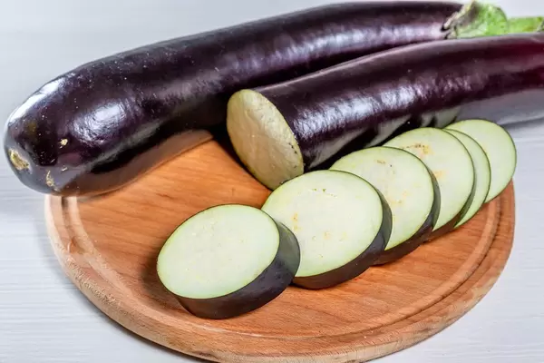 Eine Ganze und eine in Scheiben geschnittene Aubergine auf einem runden Holzbrett