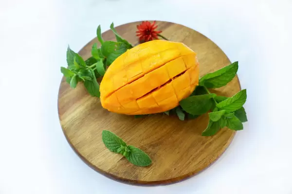 Eine geschnittene Mango mit Pfefferminzblättern auf einem runden Holzbrett