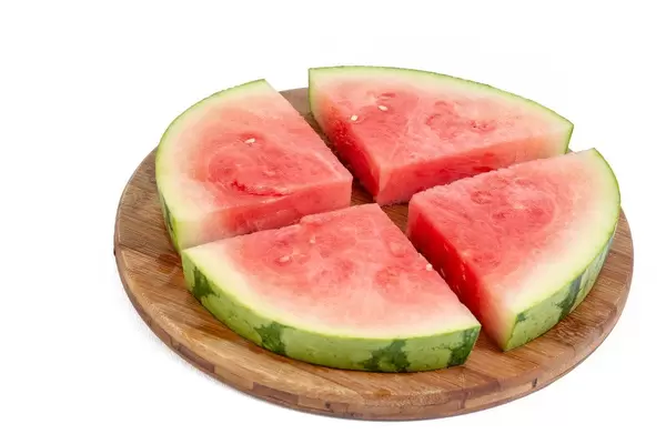 Eine geviertelte Wassermelonenscheibe, auf einem runden Holzbrettchen