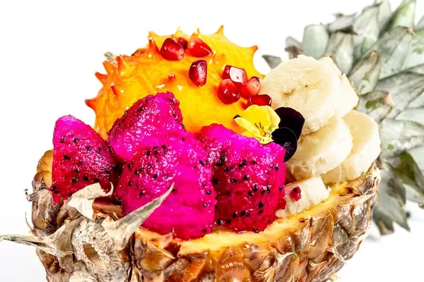 Eine halbe Ananas mit verschiedenen Fruchtstücke gefüllt. Nahaufnahme vor weißem Hintergrund