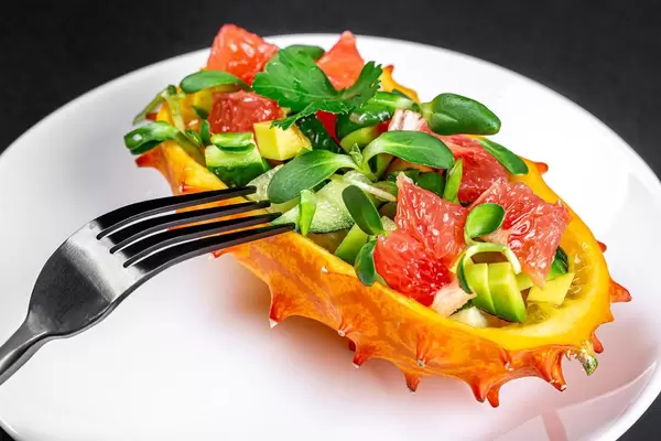 Eine halbe Kiwanofrucht gefüllt mit Avocado- und Grapefruitstückchen auf einem weißen Teller