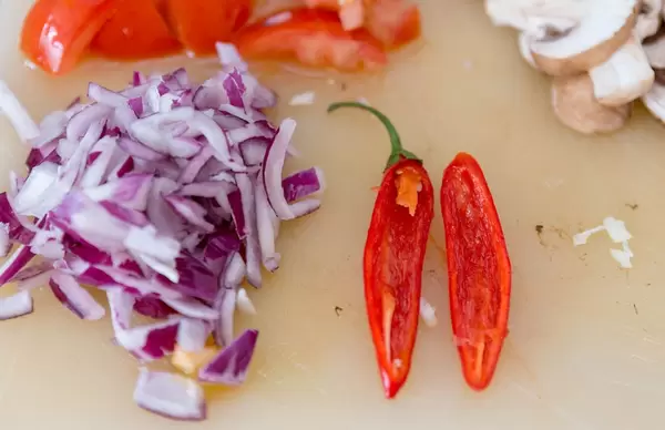 Eine halbierte rote Chilischote und gehackte rote Zwiebeln auf einem Schneidebrett