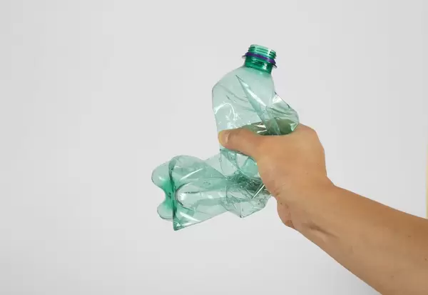Eine Hand die eine Plastikflasche zerquetscht auf weißem Hintergrund