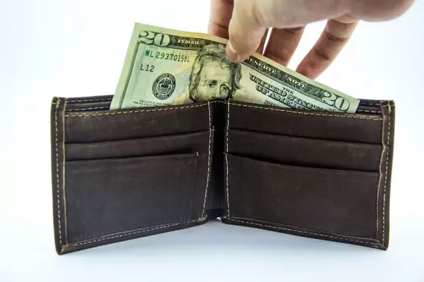 Eine Hand nimmt einen zwanzig Dollarschein aus einem dunkelbraunem Lederportmonnaie