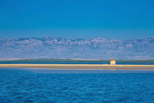 Eine kleine Holzhütte auf einem Sandstrand mit einer Berglandschaft im Hintergrund