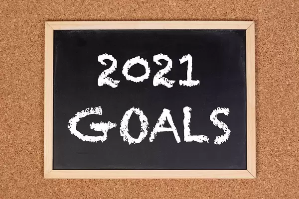 Eine Kreidetafel zeigt den Text "2021 Ziele" auf englisch, mit einer Korkwand im Hintergrund