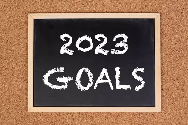 Eine Kreidetafel zeigt den Text "2023 Ziele" auf englisch, mit einer Pinnwand im Hintergrund