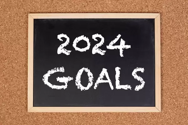 Eine Kreidetafel zeigt den Text "2024 Ziele" auf englisch, mit einer Korkwand im Hintergrund