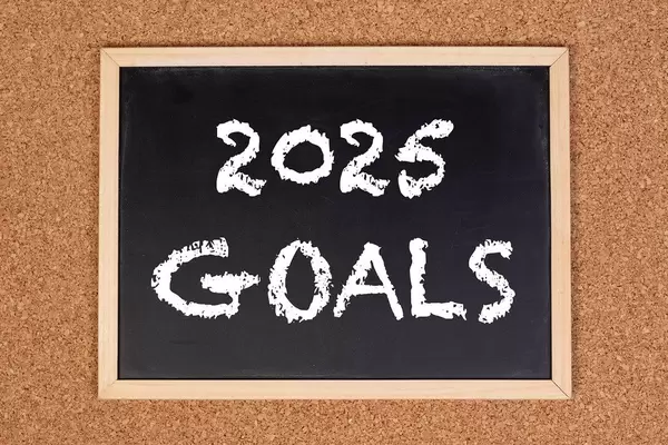 Eine Kreidetafel zeigt den Text "2025 Goals" - zu deutsch: 2025 Ziele , mit einer Korkwand im Hintergrund