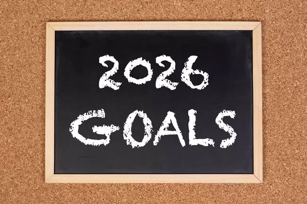 Eine Kreidetafel zeigt den Text "2026 Ziele" auf englisch, mit einer Korkwand im Hintergrund