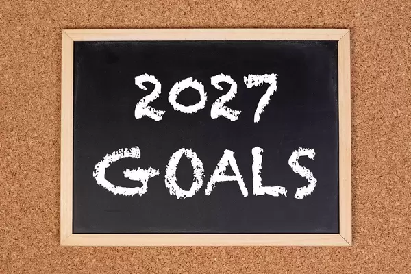 Eine Kreidetafel zeigt den Text "2027 Ziele" auf englisch, mit einer Korkwand im Hintergrund
