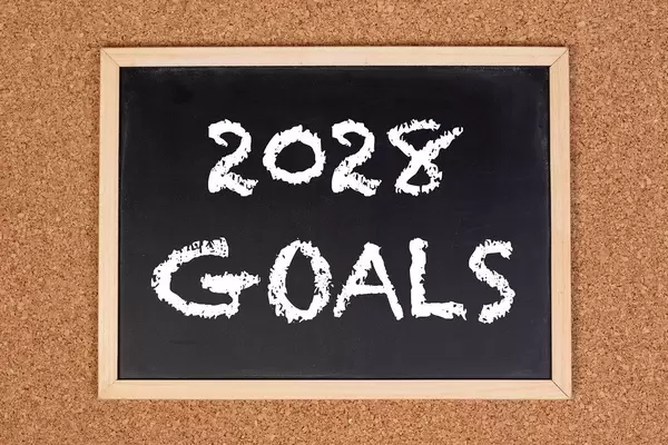 Eine Kreidetafel zeigt den Text "2028 Ziele" auf englisch, mit einer Korkwand im Hintergrund