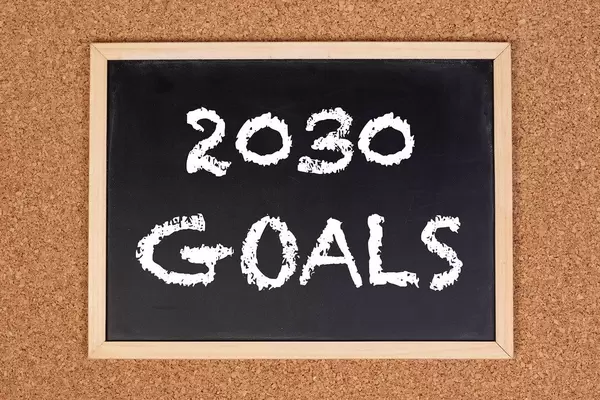 Eine Kreidetafel zeigt den Text "2030 Ziele" auf englisch, mit einer Korkwand im Hintergrund