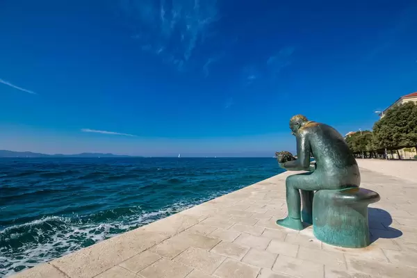 Eine Kupferstatue eines Mannes mit einer Muschel in den Händen an einer Promenade