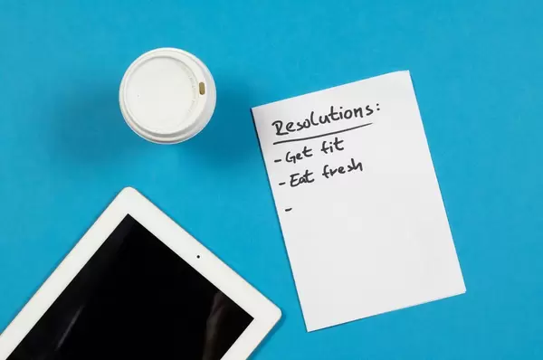 Eine Liste mit Neujahrsvorsetzen, einem Becher Kaffee und iPad auf blauem Hintergrund