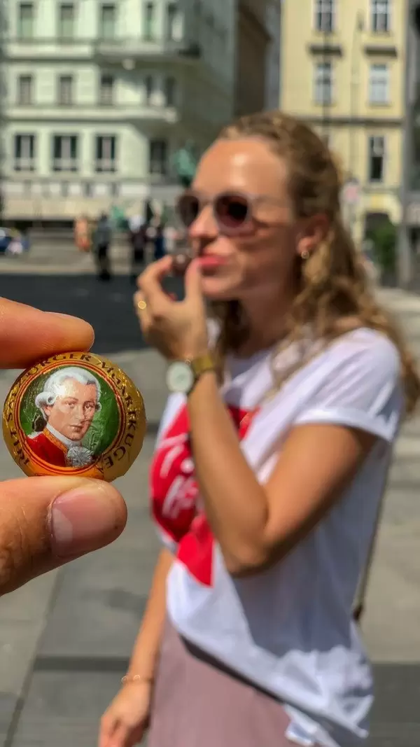 Eine Mozartkugel zwischen den Fingern, junge Frau im unscharfen Hintergrund