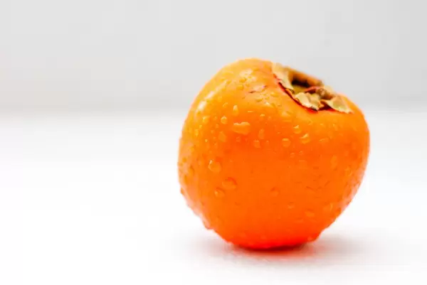 Eine nasse Kaki-Frucht vor weißem Hintergrund