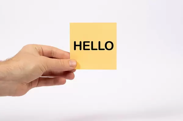 Eine Notiz mit der Aufschrift Hello  in der Hand gehalten auf weißem Hintergrund