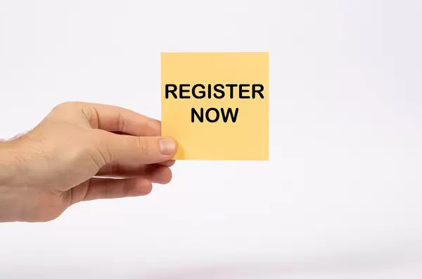 Eine Notiz mit der Aufschrift Register Now in der Hand gehalten auf weißem Hintergrund