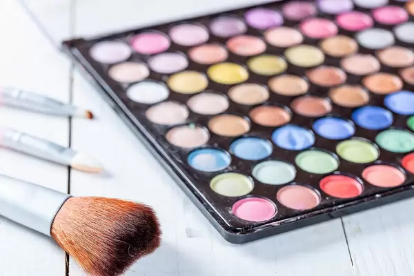 Eine Pallete mit buntem Liedschatten und ein Schminkpinsel auf weißem Hintergrund