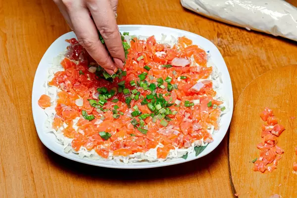 Eine Person belegt einen Lachs Salat mit geschnittenen Frühlingszwiebeln