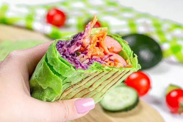 Eine Person hält ein frisches Pita-Brot gefüllt mit Rotkohl, Karotten und Würstchen