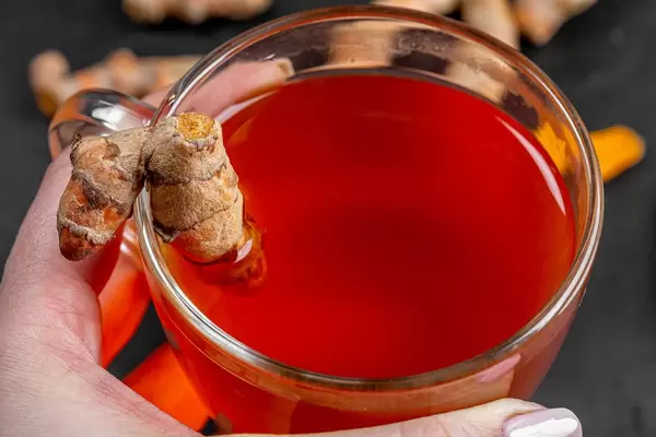 Eine Person hält eine Glastasse mit einer Kurkumawurzel Nahaufnahme