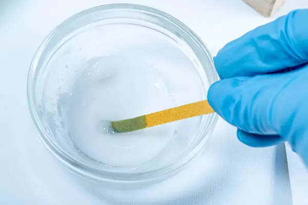 Eine Person mit Gummihandschuhen hält ein PH Indikator Teststreifen in eine Schale mit Flüssigkeit