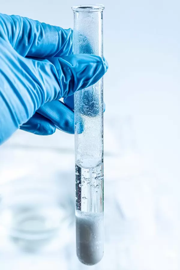 Eine Person mit Gummihandschuhen hält ein Reagenzglas zur Beobachtung einer chemischen Reaktion im Glas