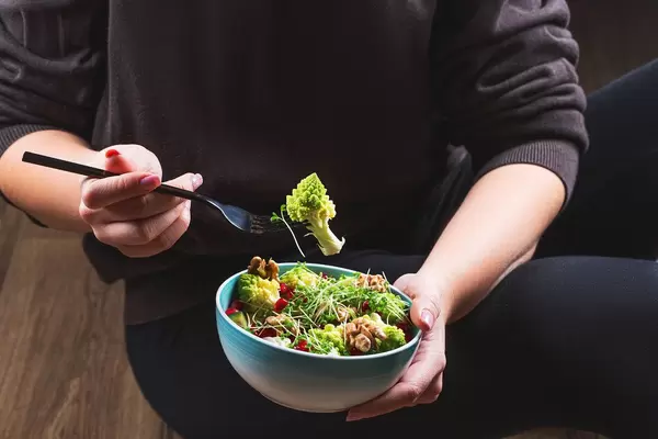 Eine Person mit schwarzer Kleidung isst einen gesunden Salat mit Romanesco Kohl, Mikrogrün und Walnusskernen