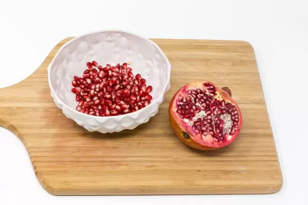 Eine Schale mit Granatapfelkernen und halbiertem Granatapfel auf Holzbrett