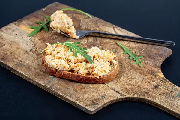 Eine Scheibe Schwarzbrot mit Rührei und Rucola auf einem Holzschneidebrett mit Gabel