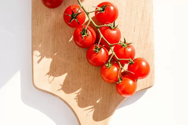 Eine Staude roter Kirschtomaten auf einem Holzbrett