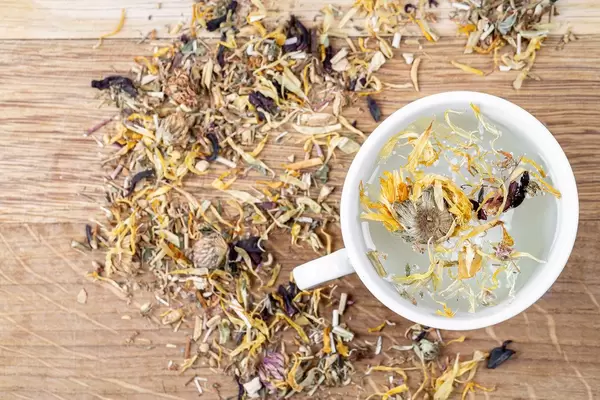 Eine Tasse frischer Grüntee mit verschiedenen Blütenblättern. Aufnahme von oben
