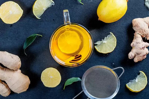 Eine Tasse Tee mit Zitronenscheiben, Ingwerwurzeln, Teeblättern und einem Teesieb auf schwarzem Hintergrund
