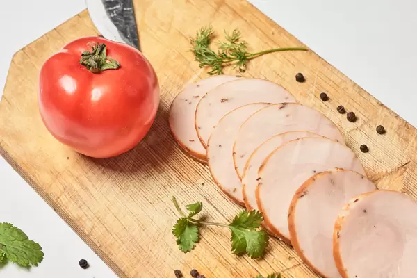 Eine Tomate und einige Scheiben von geräuchertem Hähnchen-Fleischwurst auf einem Holzschneidebrett
