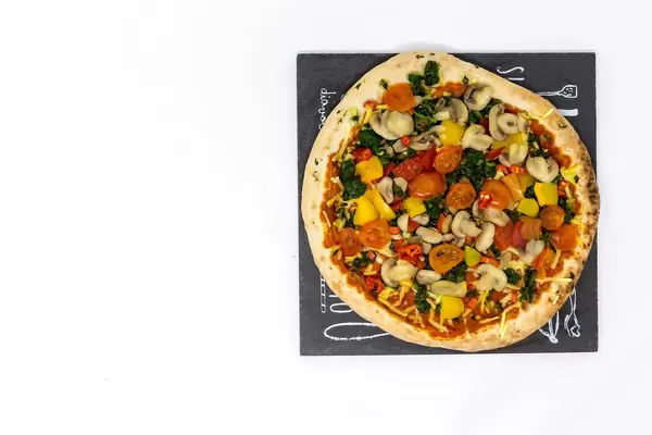 Eine vegane Pizza mit Champignons, Spinat, Paprika und Tomaten auf einem Schild - Aufsicht